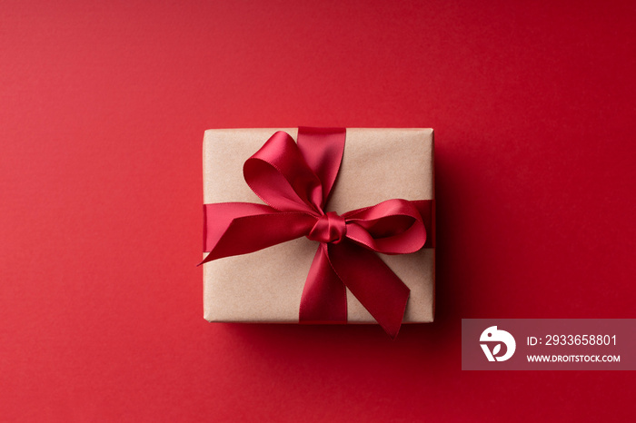 Top view on Christmas gift box with red bow on red background.