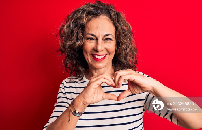 Middle age beautiful brunette woman wearing striped t-shirt standing over red background smiling in 