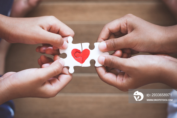 Two kid hands connecting couple jigsaw puzzle piece with drawn red heart