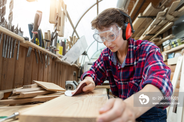 Young attractive 30-40 professional female carpenter looking grinding raw wood with sandpaper in car