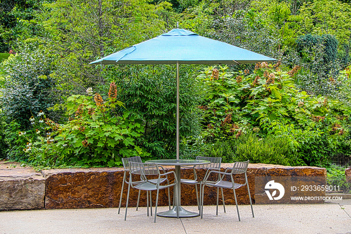 Metal outdoor table and chairs with green umbrella in front of wall made from large rocks and late s