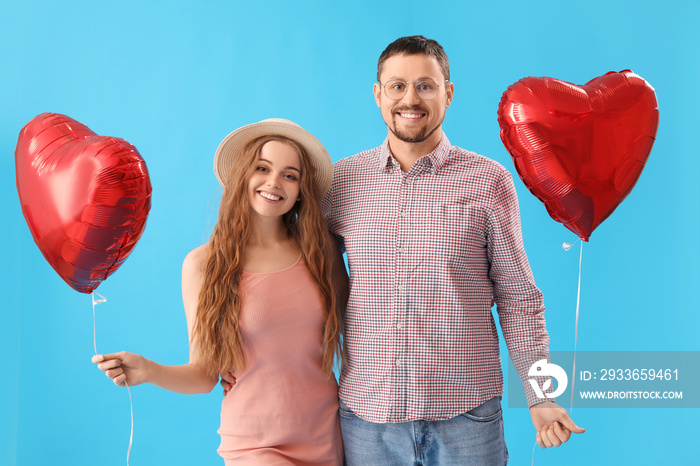 Happy young couple with heart-shaped balloons on blue background. Valentines Day celebration