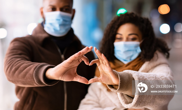 Black couple in masks making heart shape with hands