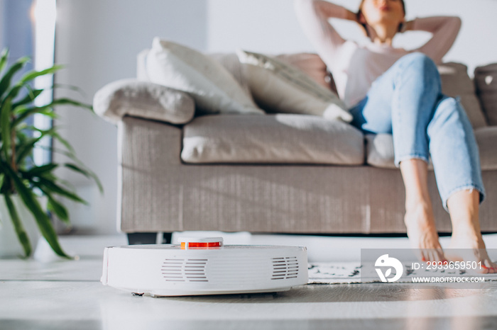 Woman relaxing on sofa while robot vacuum cleaner doing housework