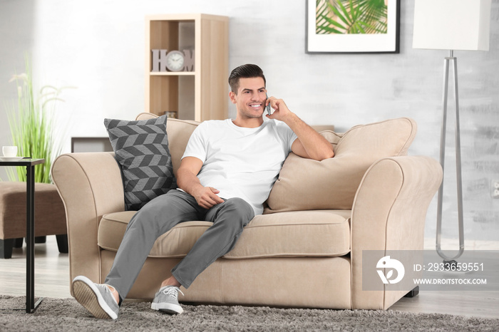 Handsome man speaking by cellphone while resting on sofa at home