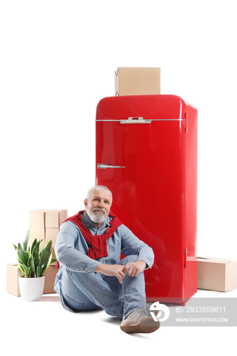 Mature man with moving boxes and red fridge on white background