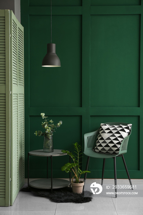 Stylish glass vase on table near chair in interior of green living room