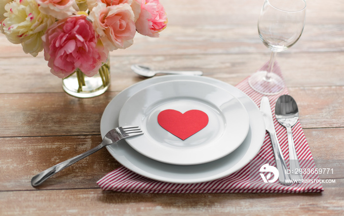 valentines day, table setting and romantic dinner concept - close up of plates with cutlery, flowers