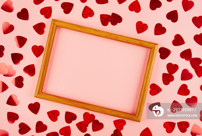 Flat lay view at wooden frame among heart shaped tinsel on pink background