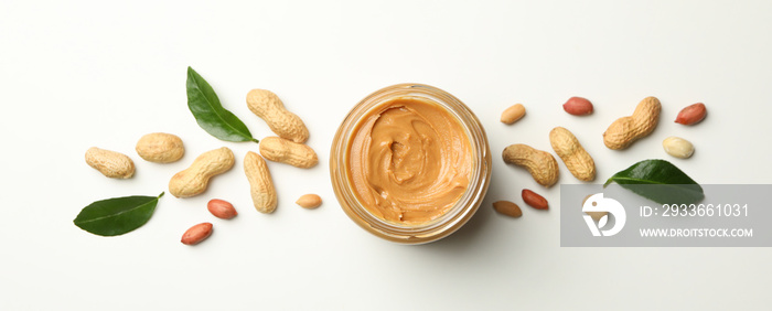 Jar with peanut butter, peanut and leaves on white background