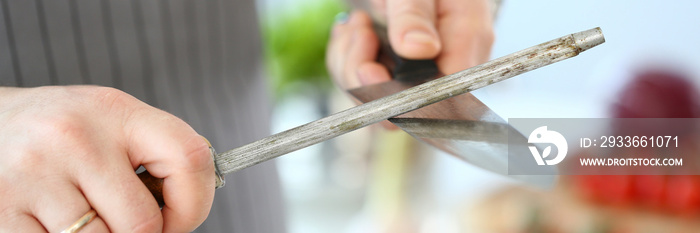 Chef Male Sharpening Stainless Knife Photography. Man Whetting Steel Blade in Kitchen Manually. Male Preparing Kitchenware for Cooking. Holding Sharp Culinary Object in Hands Partial View Shot