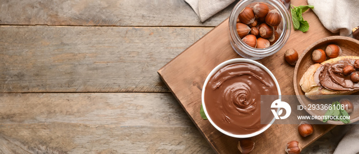 Bowl with tasty chocolate butter and hazelnuts on wooden background with space for text