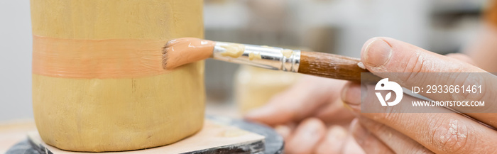 Cropped view of craftsman painting on ceramic sculpture in workshop, banner.