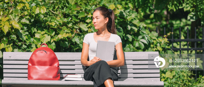 University student sitting on park bench on campus holding laptop. Panoramic of Asian young woman with backpack, books, looking to the side.