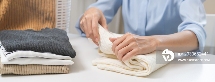 Housewife, asian young woman hand in many folding freshly shirts, sweaters or dress on desk, table after washing clean clothes and drying, making household working in room at home. Laundry and maid.