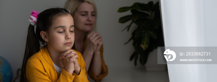 Mother and her daughter reading from bible and praying in their knees near the bed