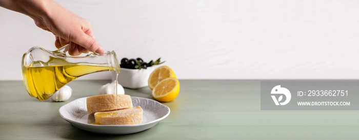 Woman pouring tasty olive oil from bottle onto fresh bread