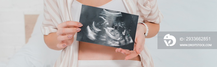 Cropped view of pregnant woman holding ultrasound scan of baby on bed, panoramic shot