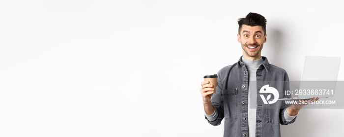 Happy energized guy drinking coffee and working on laptop, got energy from drink, standing on white background