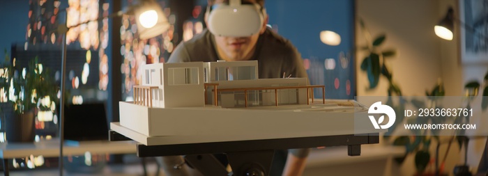 Portait of Caucasian male architect or student using a virtual reality VR headset to work on a house project late at night, preparing for presentation with a client