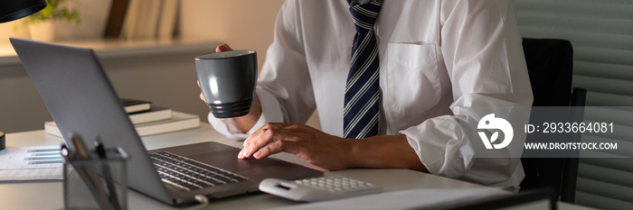 Overwork Concept An office man who works late drinking a cup of coffee while concentrating on his work on the notebook