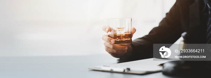 A lawyer holding a glass of whiskey, He’s in his office, and he’s stressing about arguing for a client, he’s a lawyer. The concept of clear legal litigation.