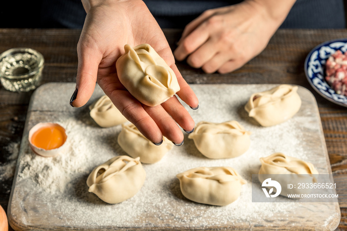 Uzbek national food manta, like dumplings, on a wooden board, lie in flour with an egg. Hand holds manta