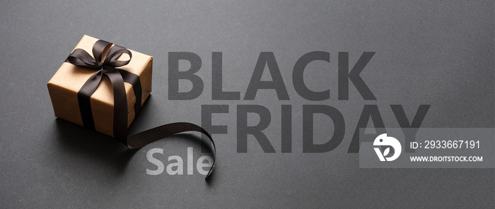 Black Friday Sale text lettering and a gift box with a ribbon bow, dark background.