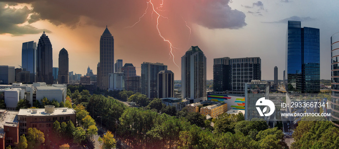 an aerial panoramic shot of the skyscrapers and office buildings in the city skyline surrounded by lush green trees with storm clouds and lightning in downtown Atlanta Georgia USA