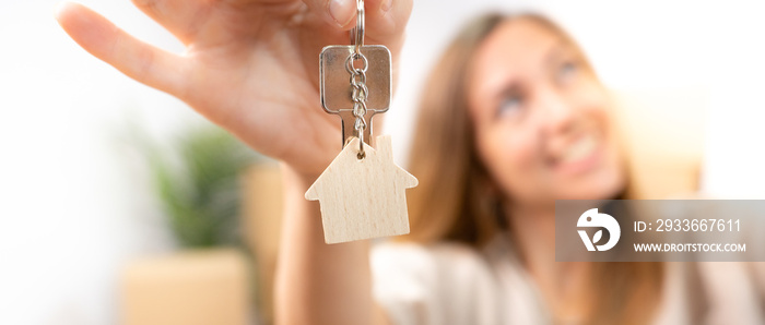 Happy young woman smiling with the new home keys keychain with wooden house real state banner. High quality photo