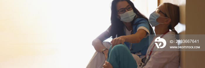 Surgeon in hospital corridor with communicates with doctor sitting on floor