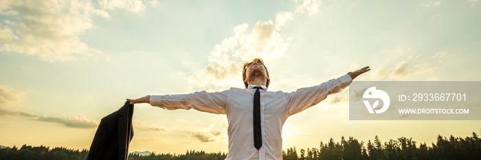 Powerful young businessman standing under evening sky