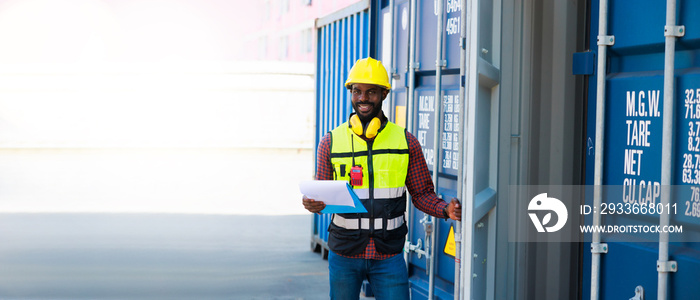 Portriat handsome male African American Industrial and factory Specialist. Black man worker wearing yellow protective hard hat helmet working at container yard.