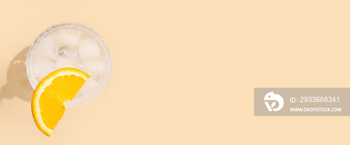 Glass with a cocktail with an orange slice on a beige background. Top view, flat lay. Banner