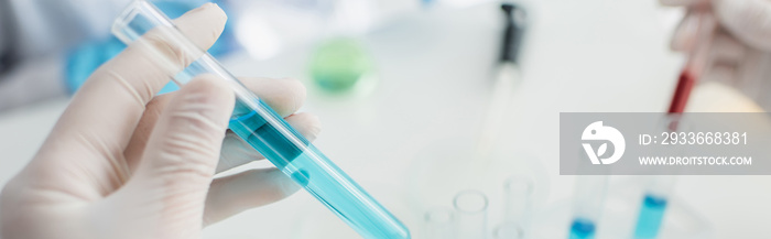 partial view of scientist in latex glove holding test tube with blue liquid, banner.