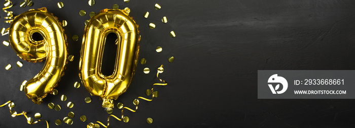 golden foil balloon number ninety. Birthday or anniversary card with the inscription 90. Black concrete background. Anniversary celebration. Banner.