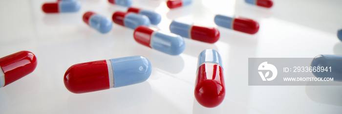 Lot of blue and red capsules lying on white table closeup background