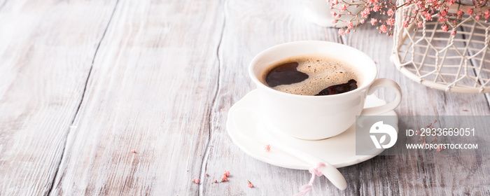 White cup of coffee with pink flowers on old white wooden background with copy space.