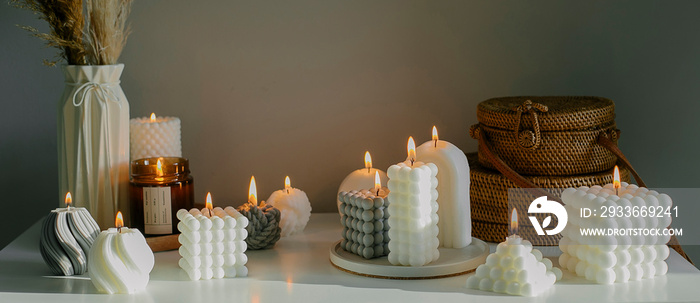 Banner image. Home interior decor. White dresser with dried flowers in vase, rattan bags and variety candles. Still life, hygge concept