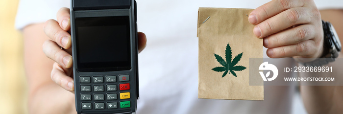 Close-up of courier holding paper package with traditional meds. Cannabis in bag with leaf symbol. Cashier machine for fast payment. Nfc technology counter and remedy concept