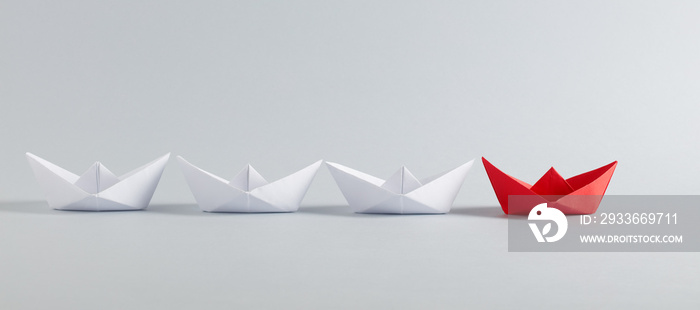 Red paper boat leads white paper ships. Leadership, collaboration, cooperation, or partnership in business