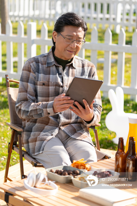 一个老年男人坐在露营院子里看平板电脑