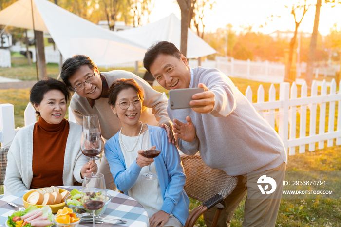 夕阳下中老年朋友在庭院里聚会喝酒拍照片