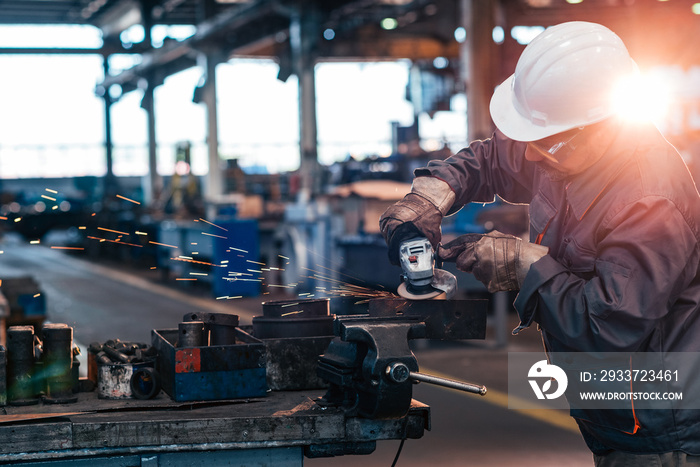 Mature worker working with metal parts and grinder at factory workshop.