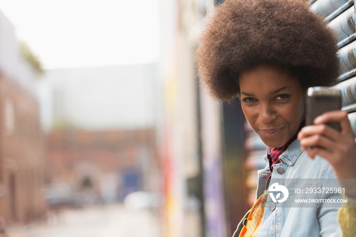 Portrait playful young woman with afro taking selfie on city street