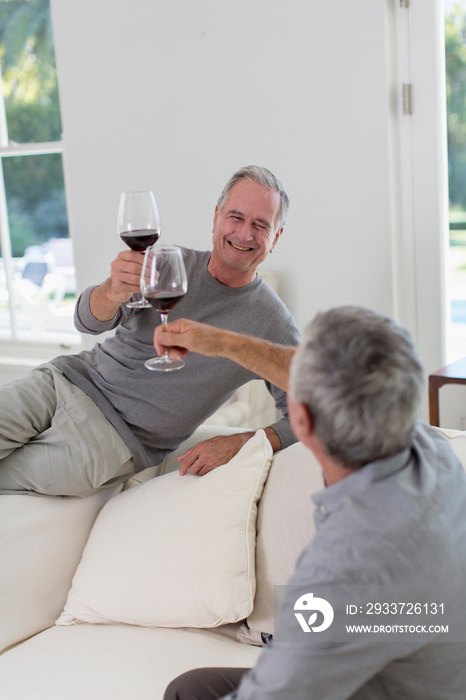 Senior men friends toasting red wine on sofa