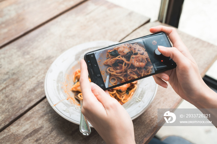 Female blogger photographing lunch in restaurant with her phone. A young woman taking photo of spagh