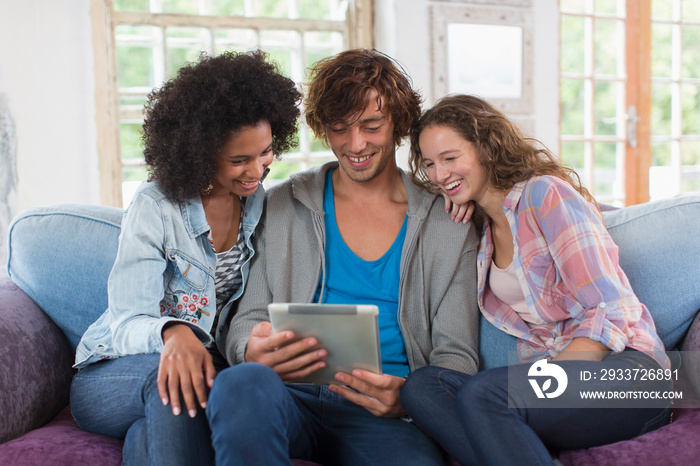 Young friends using digital tablet on sofa