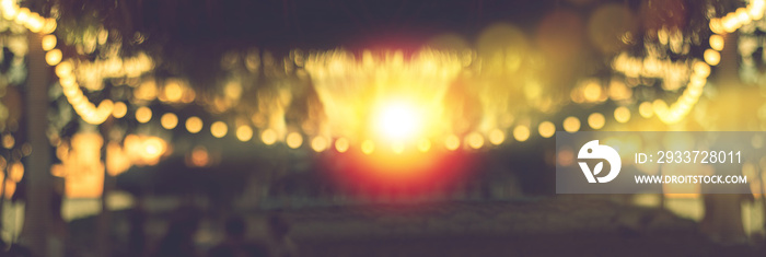 blurred bokeh light on sunset with yellow string lights decor in beach restaurant