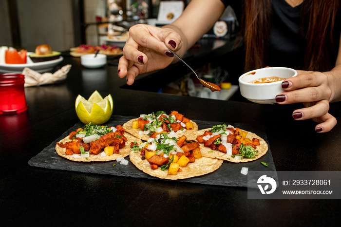 Hand salseado tacos al pastor on a slate plate on the counter of a Mexican restaurant